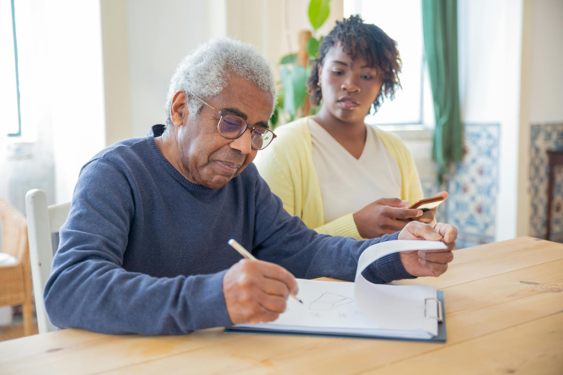 Older adult signing document at table with another person looking on. Elderly care services in Lancaster, CA.