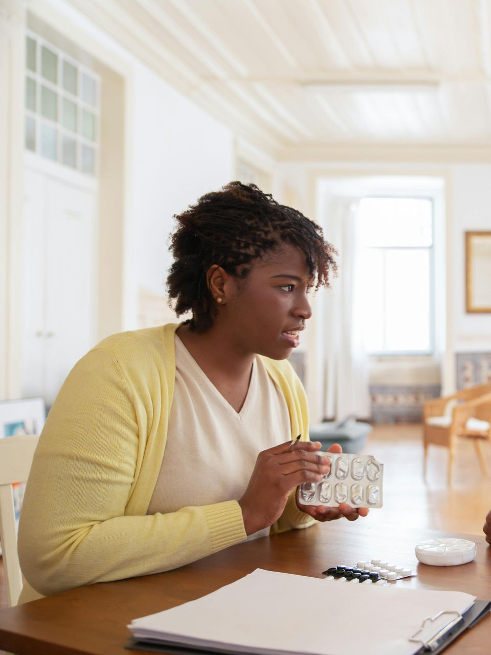 Woman with dark hair gestures with a medication blister pack. Elderly home care in Lancaster, CA.