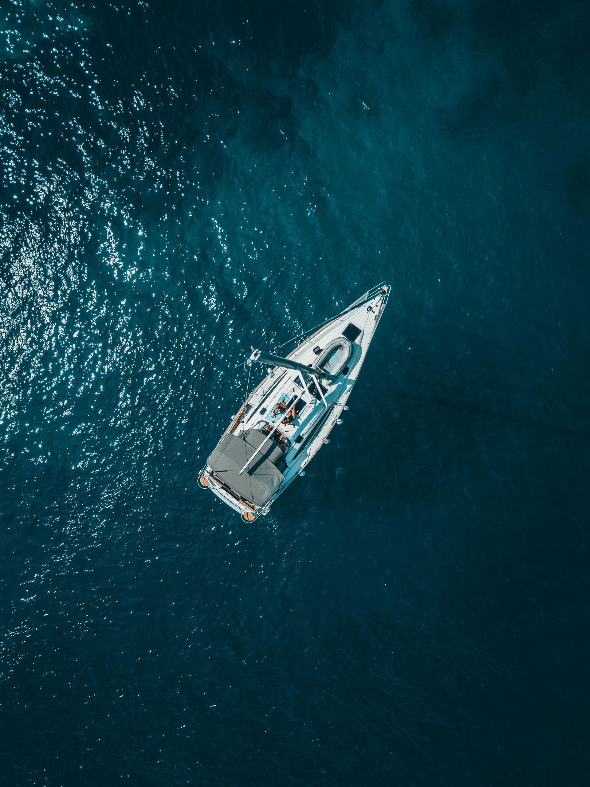 Sailboat on deep blue water, overhead view.