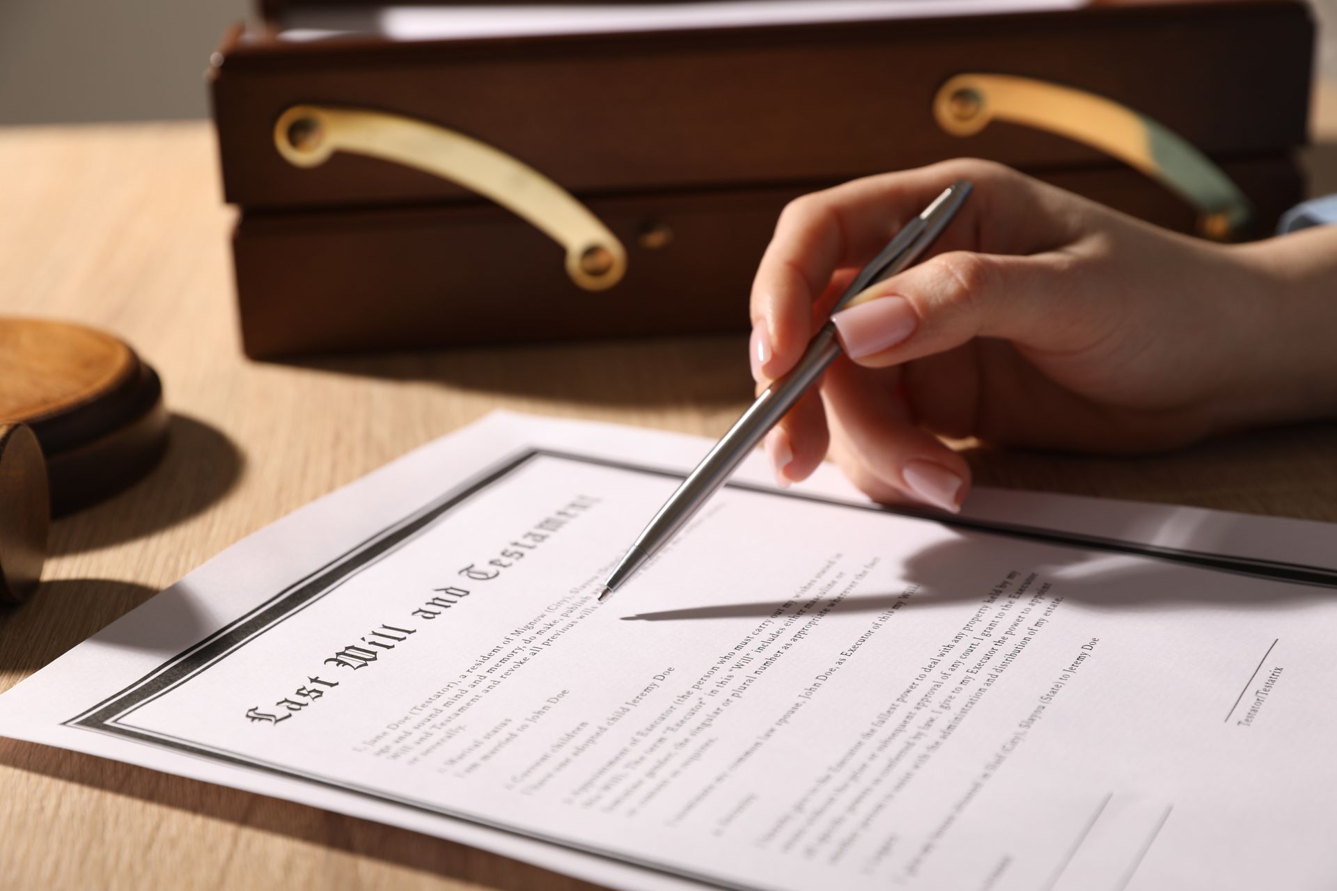 Hand holding a pen over a last will and testament document on a wooden desk with a legal briefcase nearby. Hand holding a pen over a last will and testament document on a wooden desk with a legal briefcase nearby.