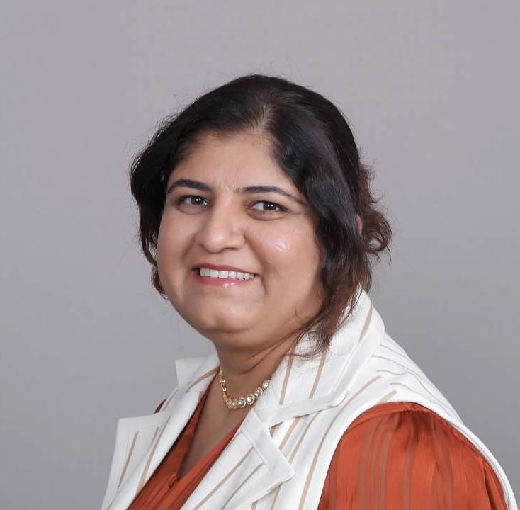 A woman wearing a white vest and a necklace smiles for the camera