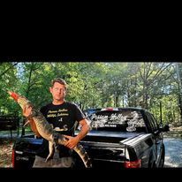A man is holding a large fish in front of a truck.