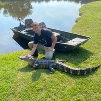 A man is kneeling next to an alligator next to a boat.