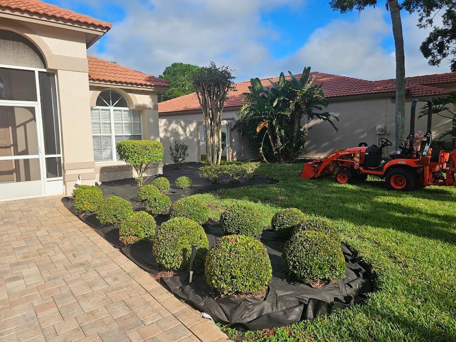 Front yard with trimmed shrubs, stone walkway, and red lawn equipment beside a house