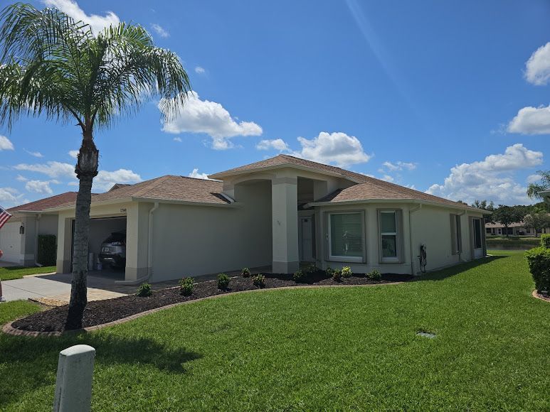 Single-story suburban house with beige exterior, palm tree, and green lawn under a bright blue sky