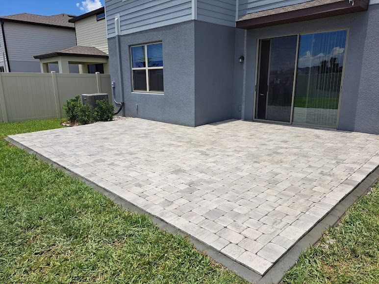 Backyard patio with light gray pavers beside a house and sliding glass door