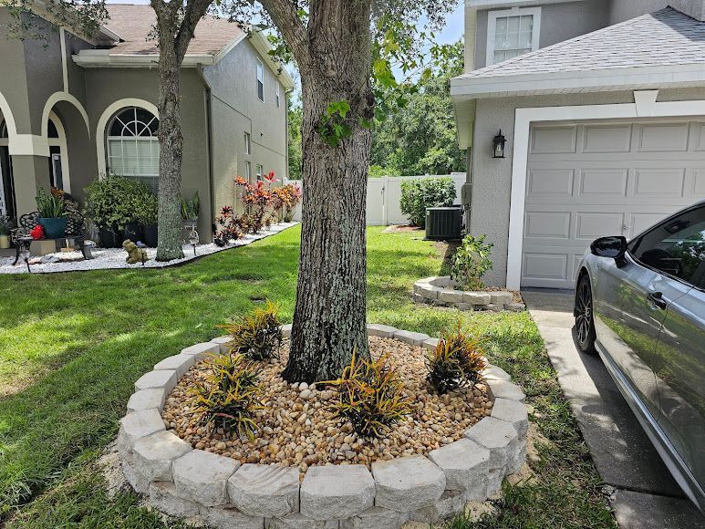 Front yard with a tree in a stone planter, landscaped lawn, and a house with a garage driveway.