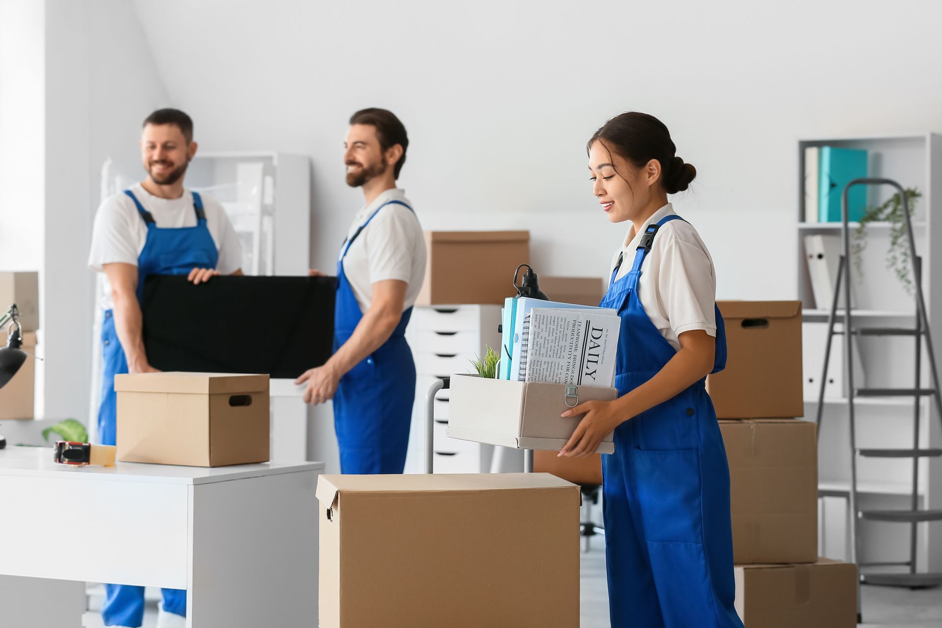 Workers in blue aprons packing boxes in a bright warehouse