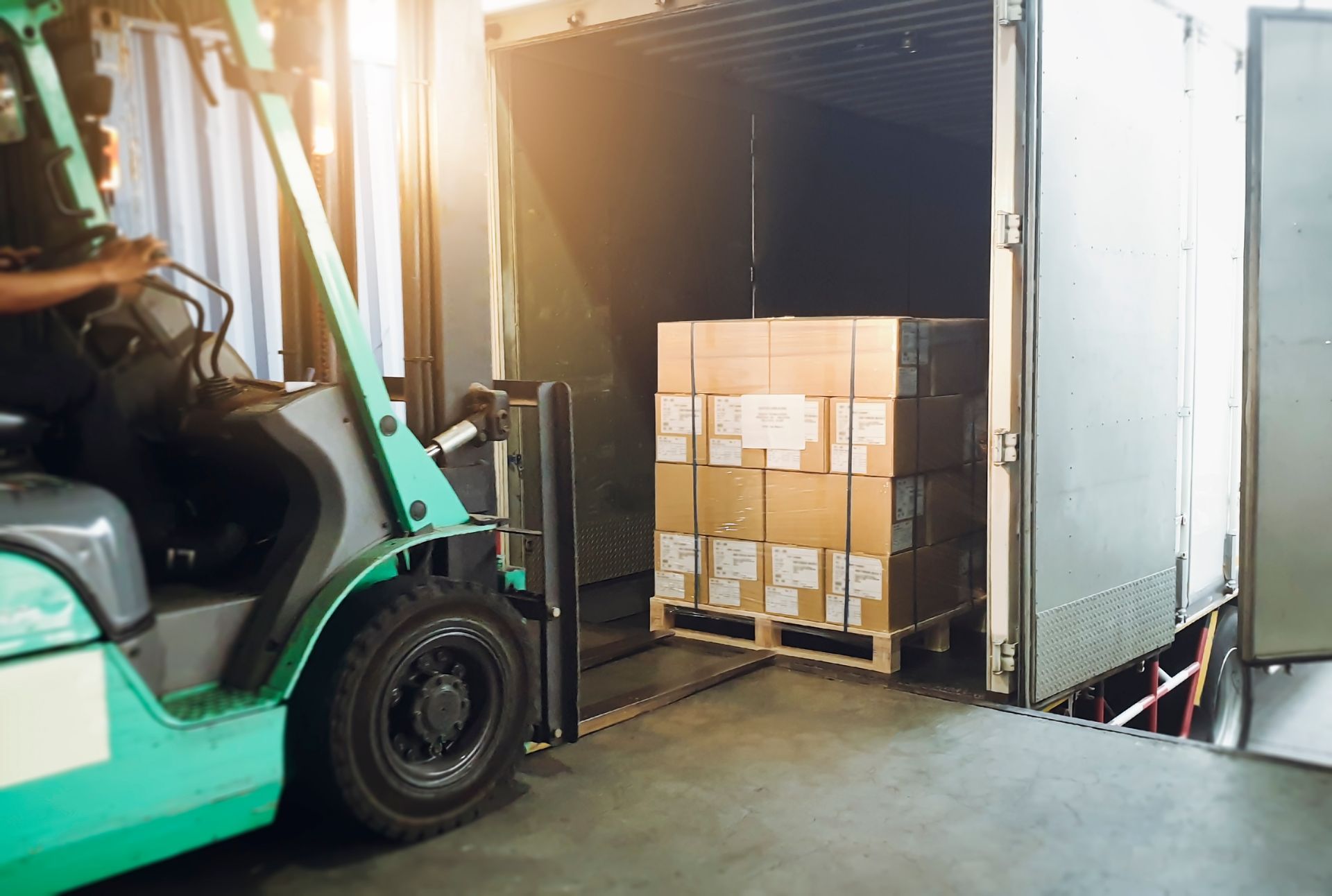 Forklift loading stacked cardboard boxes into a warehouse truck trailer.