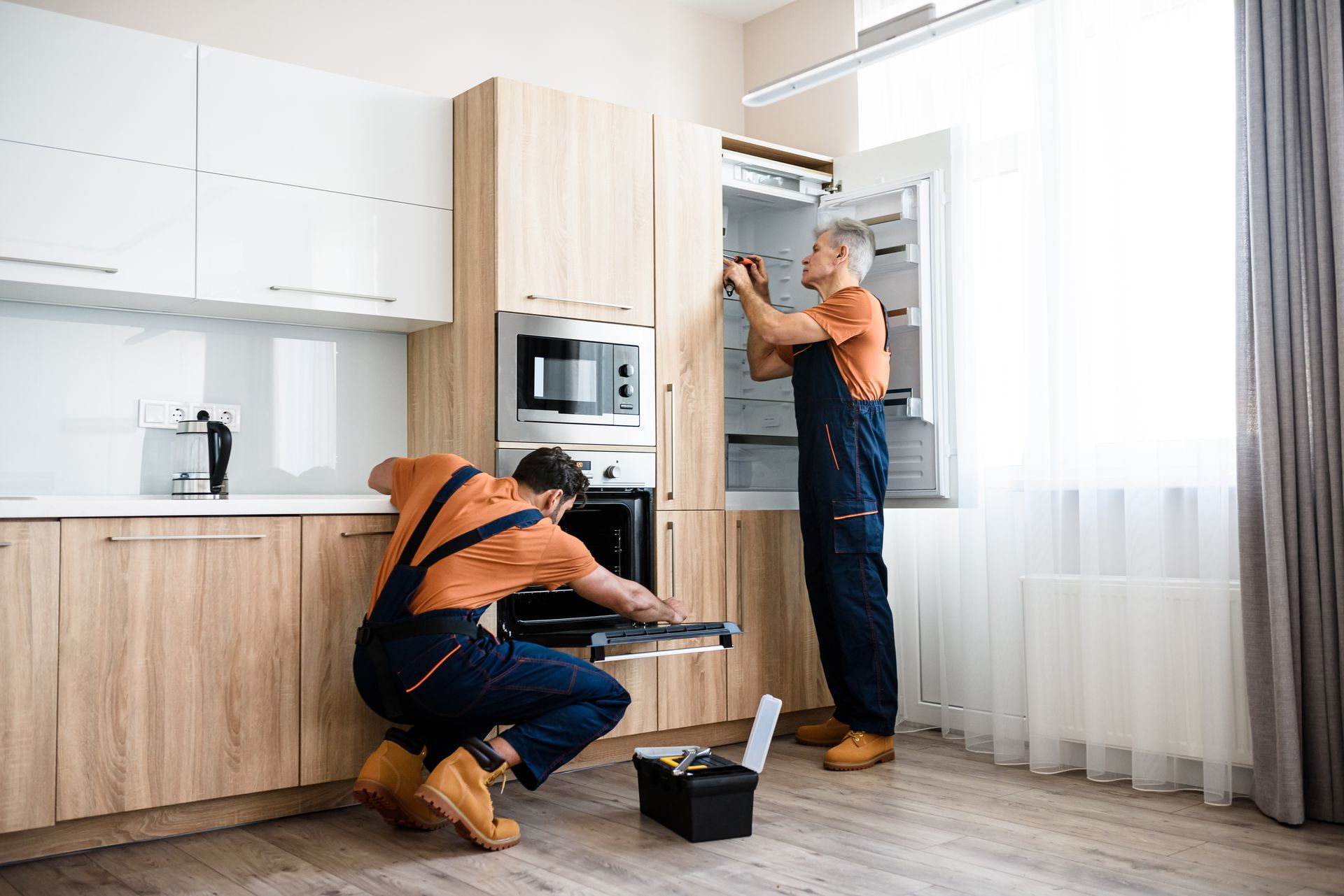Two technicians installing a kitchen cabinet beside a microwave, with tools on the floor.