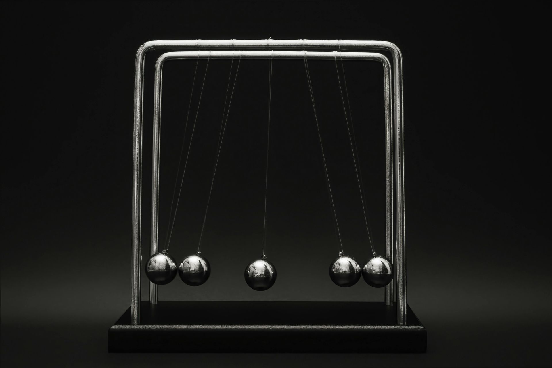 Newton's cradle with five metal balls. The leftmost ball swings, transferring momentum to the right.