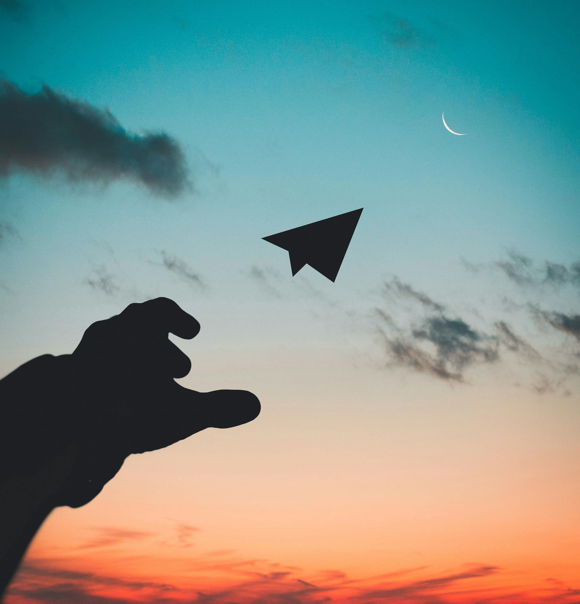 A silhouette of a hand holding a paper airplane in the sky
