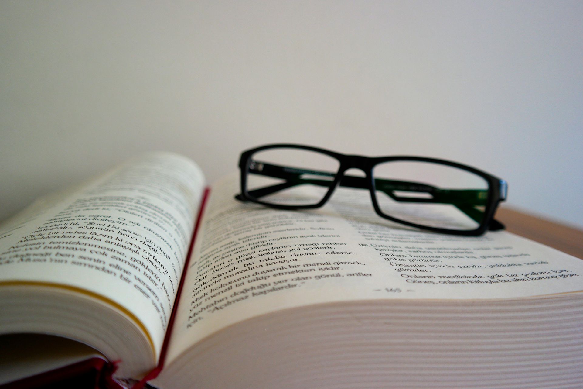 Open book with black-framed glasses resting on its pages, against a plain white background.