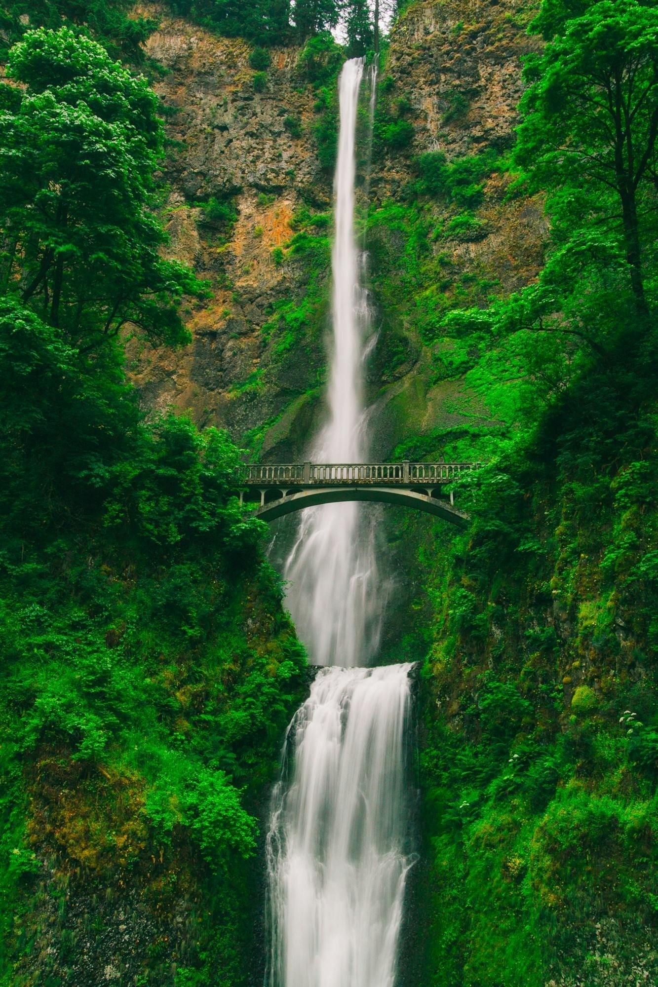 Multnomah Falls in Oregon, cascading over rocks, with a stone bridge and lush green foliage.