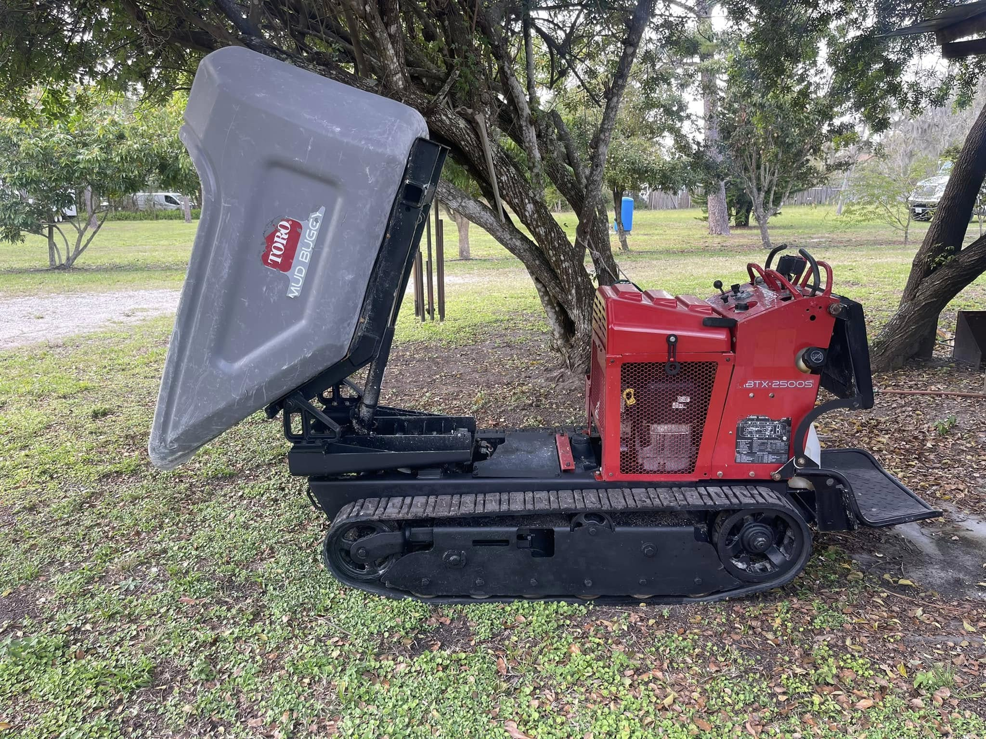 Red and gray tracked Toro dumper with raised bed, outdoors on grass.