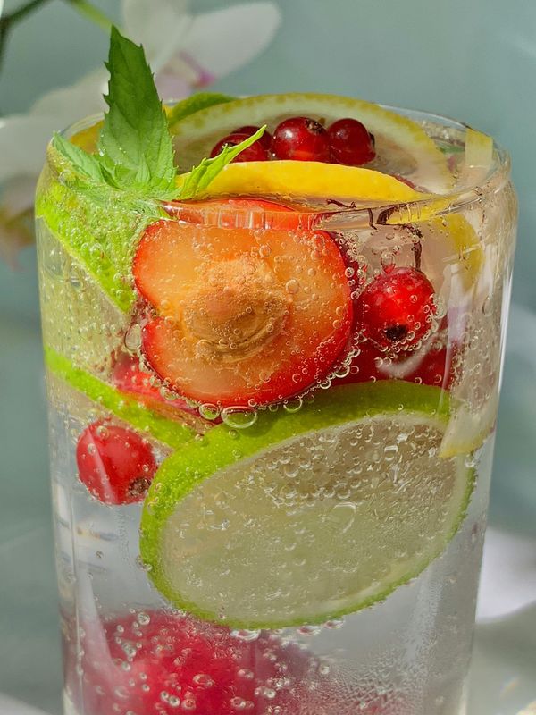 A glass of water with strawberries , raspberries , lime slices and mint leaves.