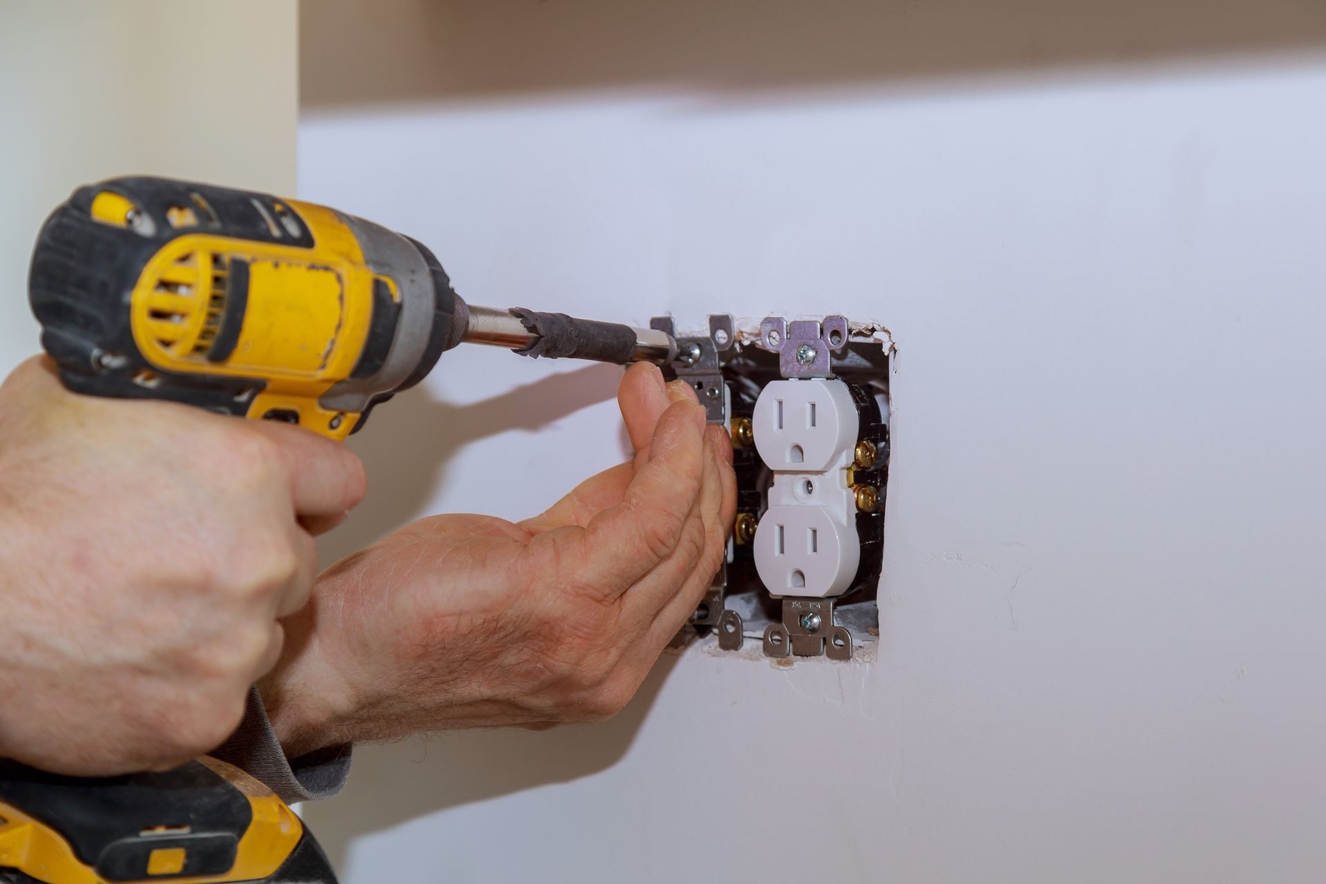 Hands installing a wall outlet with a yellow drill.