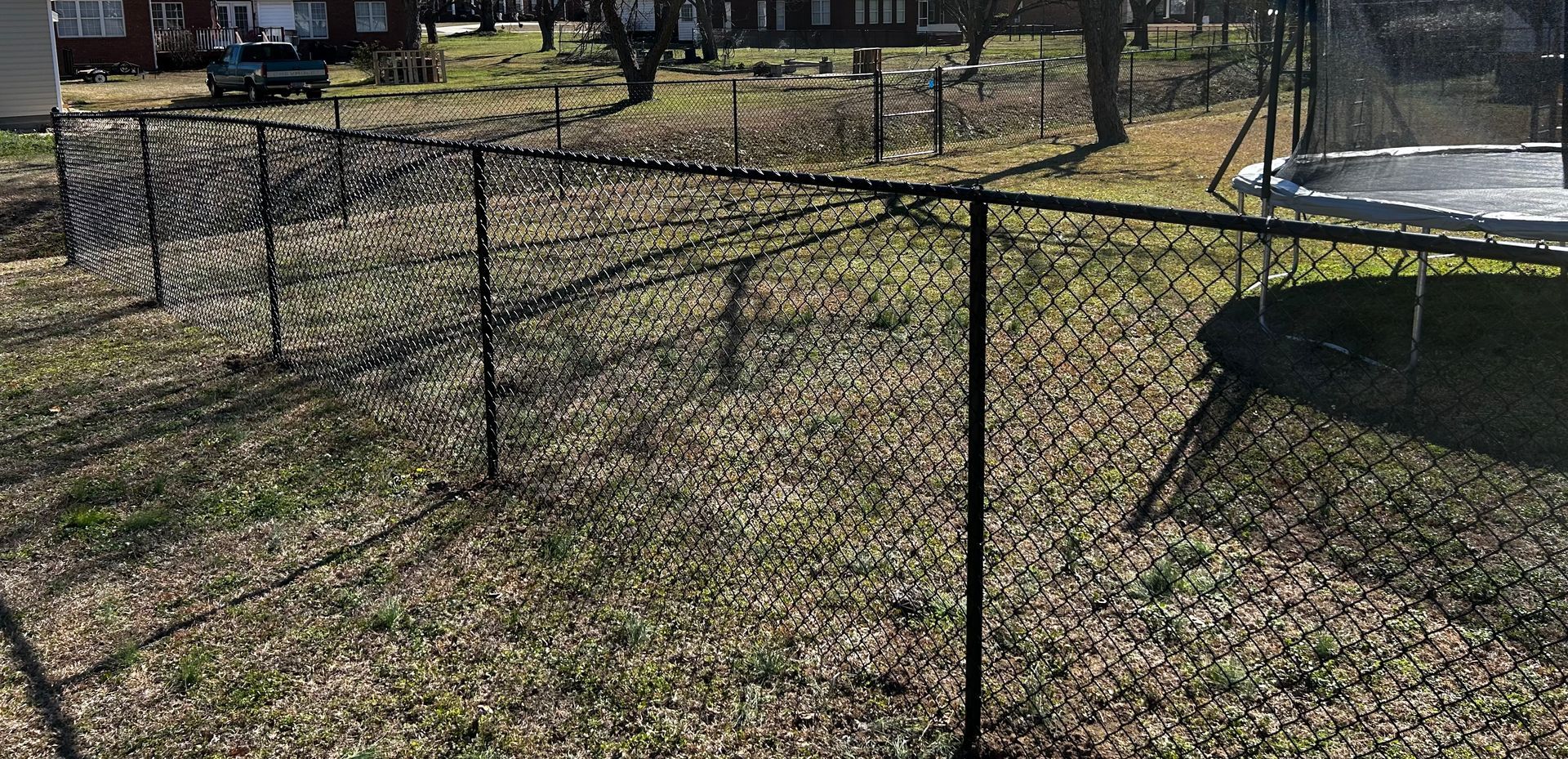 A black chain-link fence surrounds a grassy backyard with a trampoline.