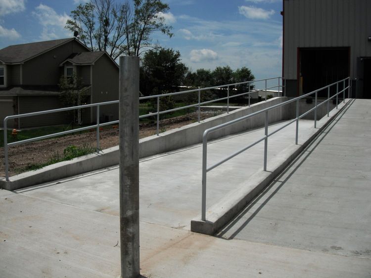 Concrete ramp with metal handrails leading to a building entrance.