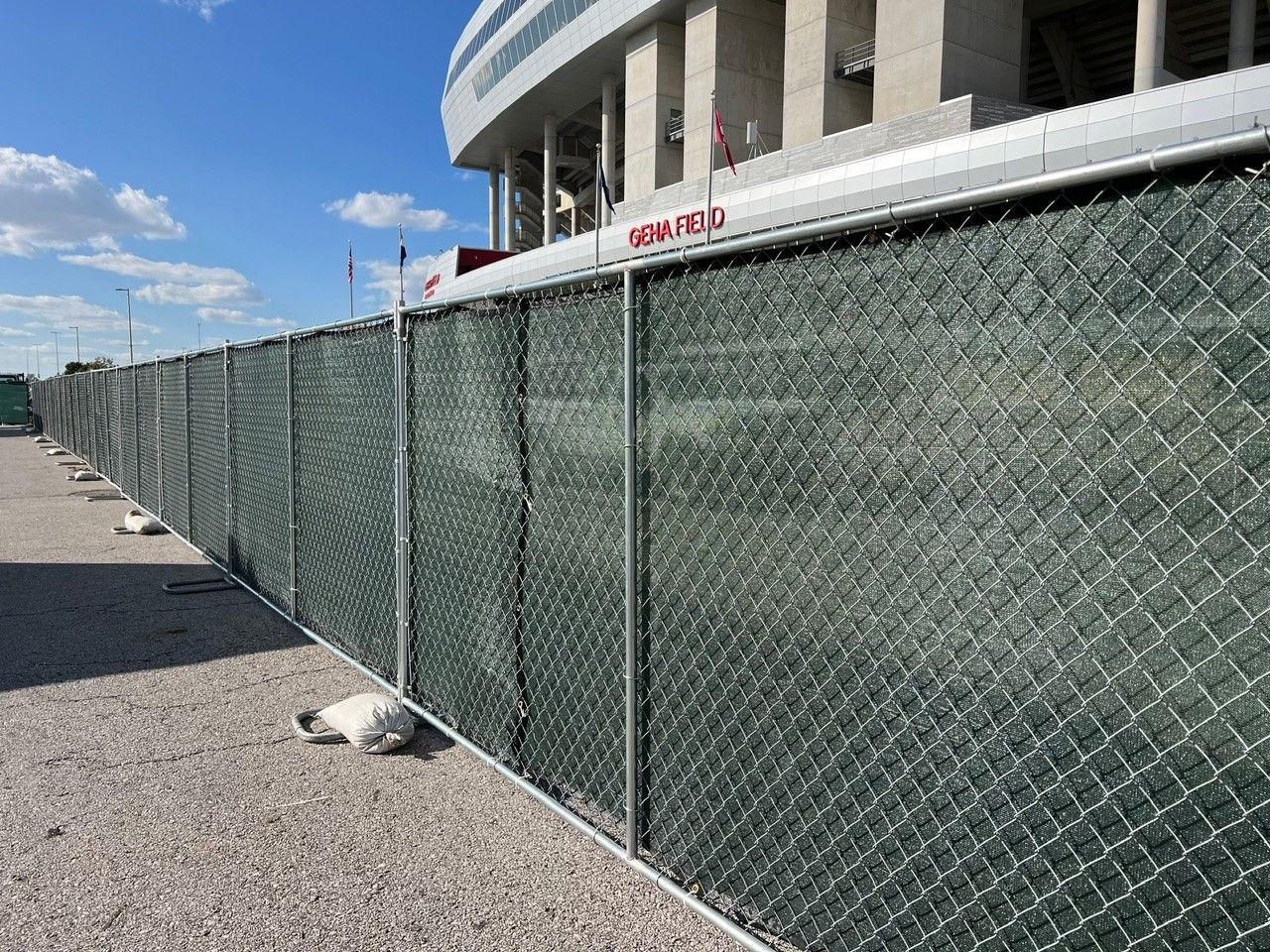 Chain link fence with green privacy screen next to a building on a gravel surface.