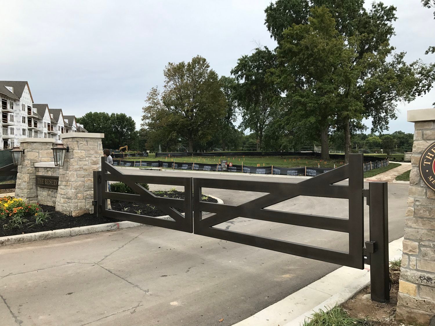 Stone pillars and dark wooden gate open to a green space and buildings.