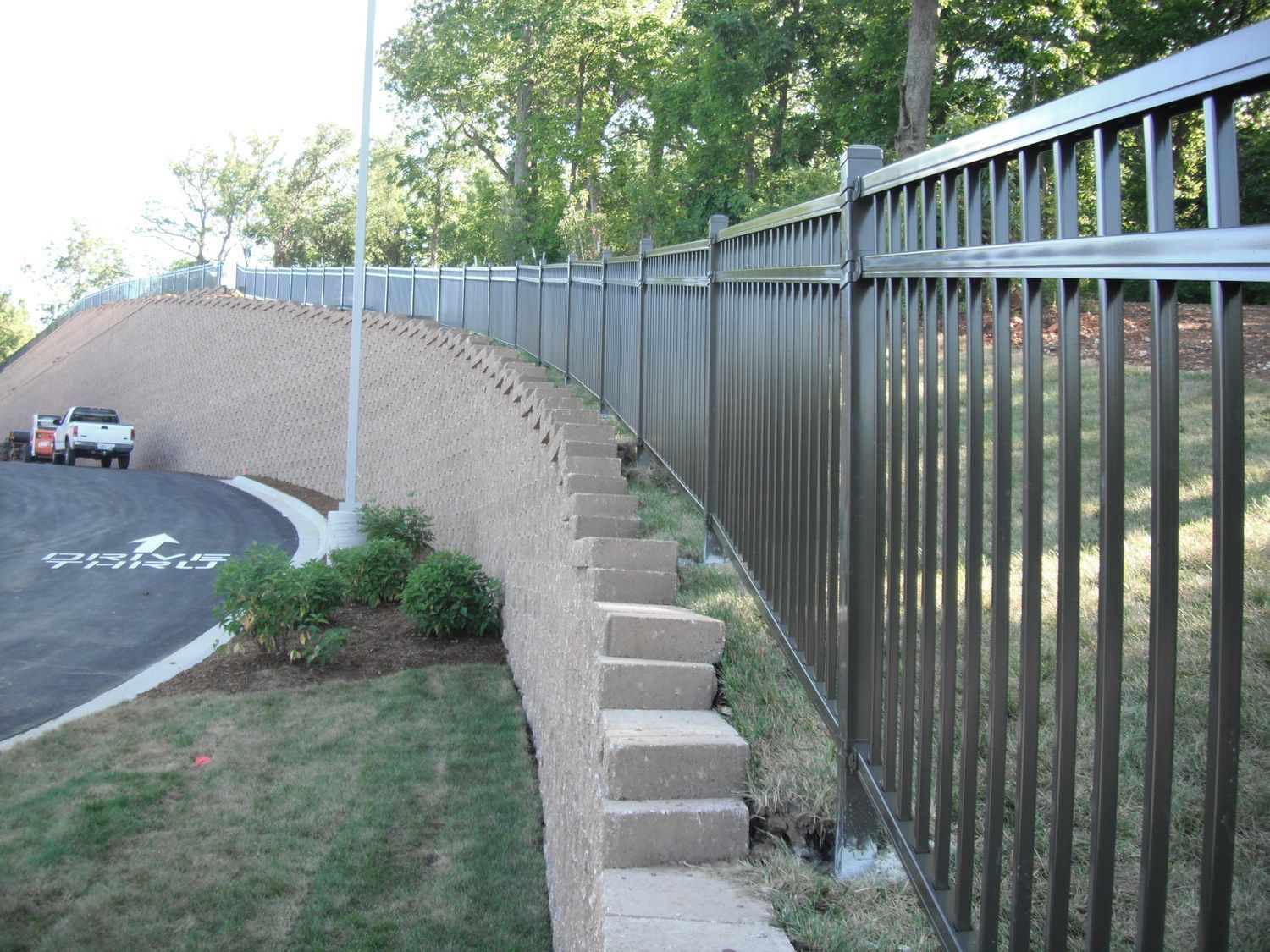 Metal fence atop a concrete retaining wall with a curved road.