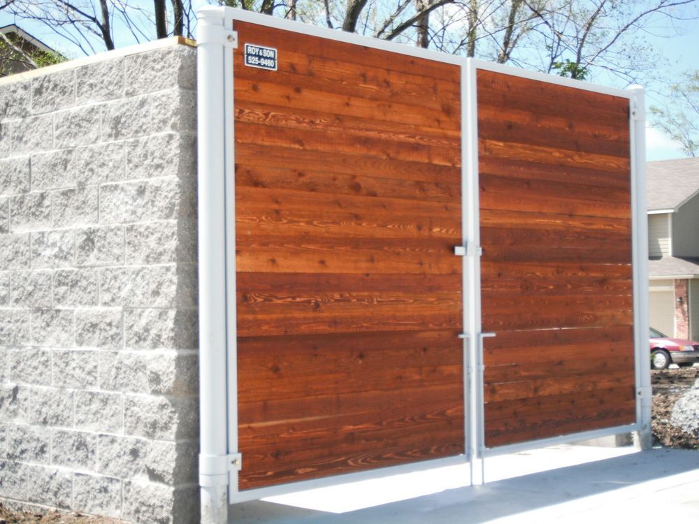 Wooden double gate in white metal frame, set against a gray brick wall.