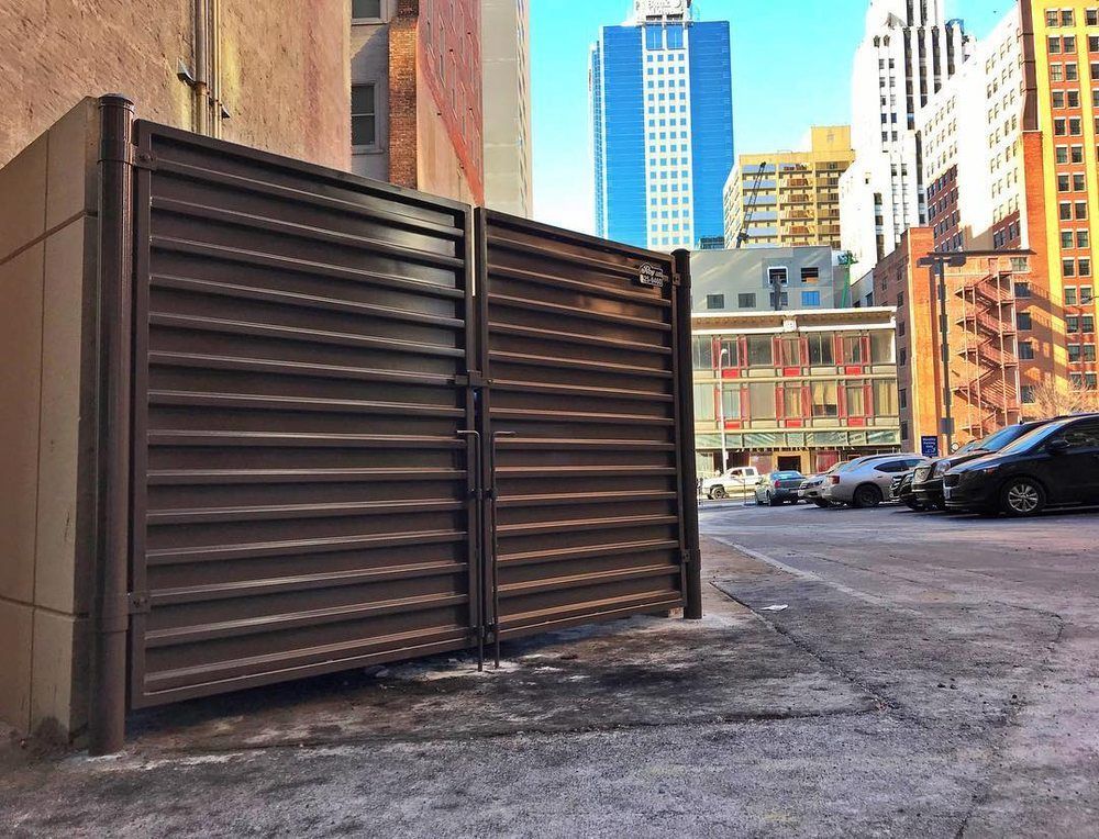 Brown metal dumpster enclosure with city buildings in the background.