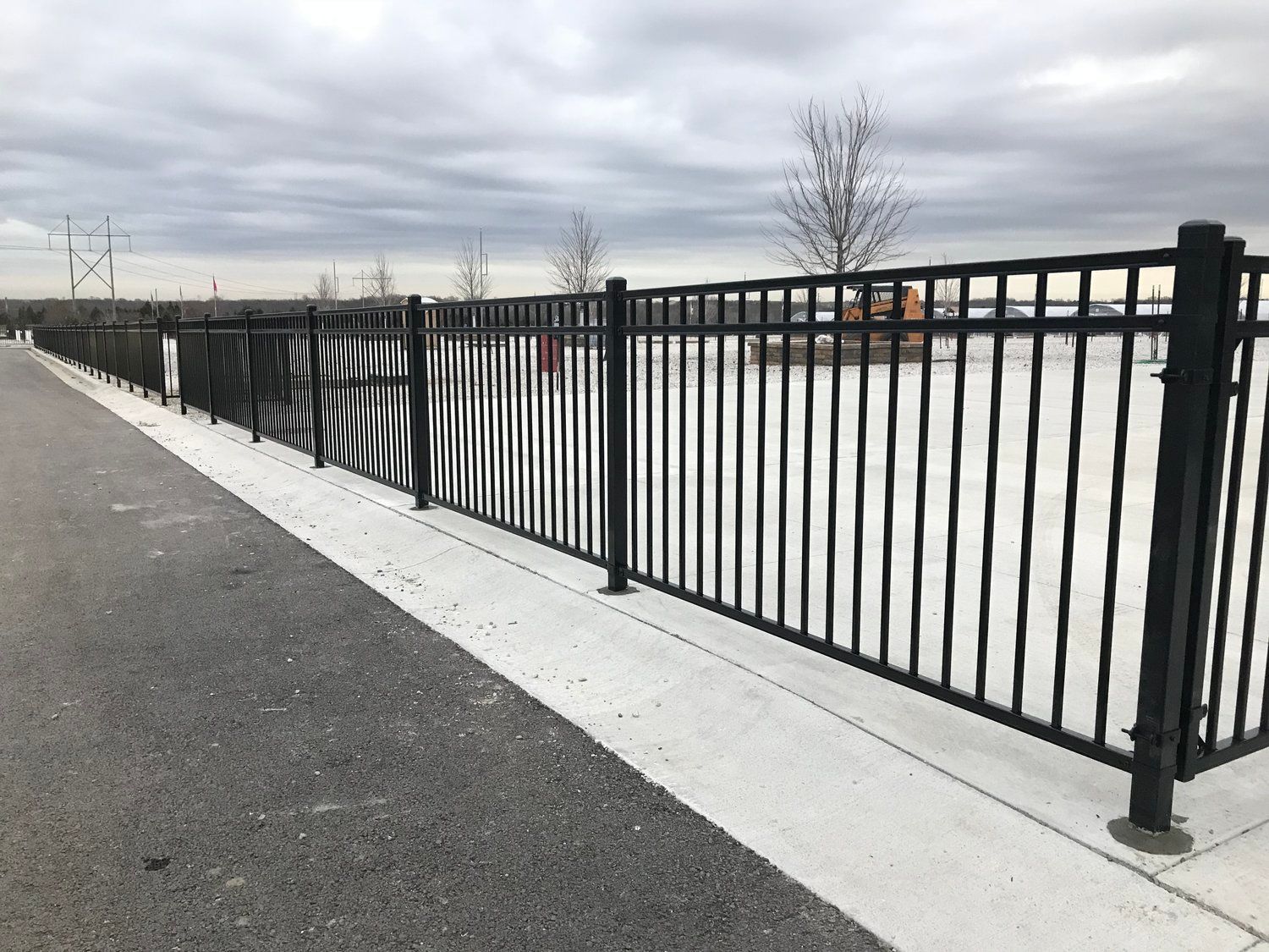 Black metal fence along a gray concrete path on a cloudy day.