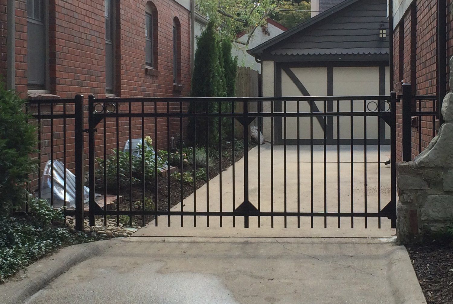 Black metal gate across a driveway, between brick buildings, leading to a garage.