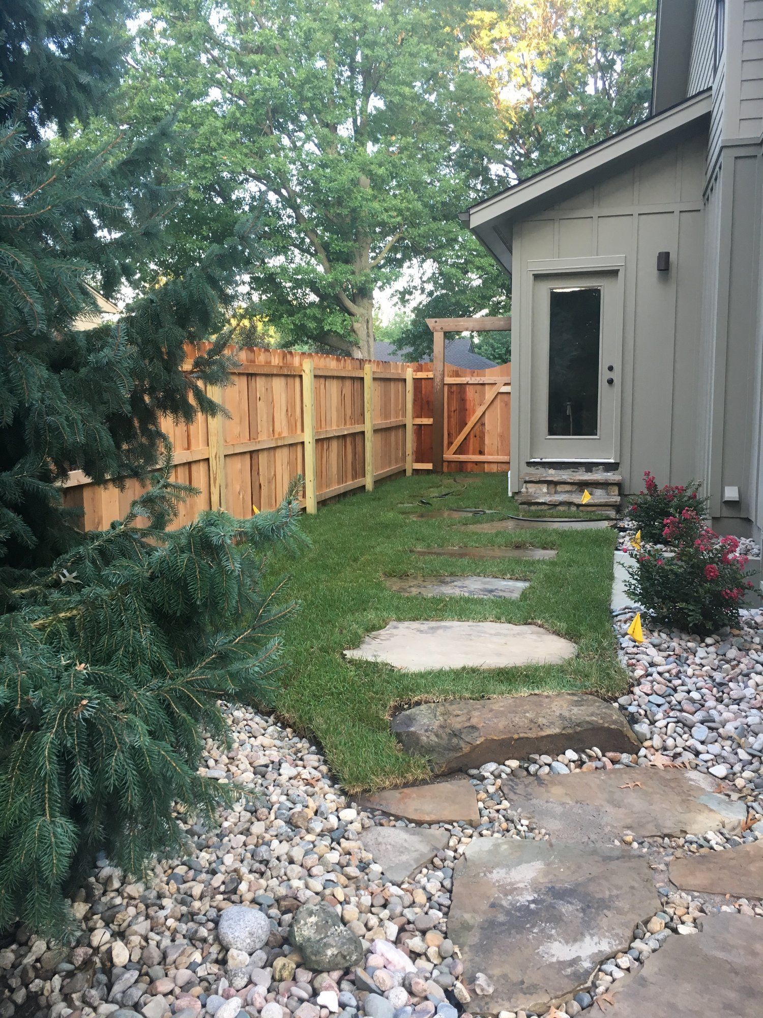 Backyard path with stepping stones, grass, wooden fence, and entry door.