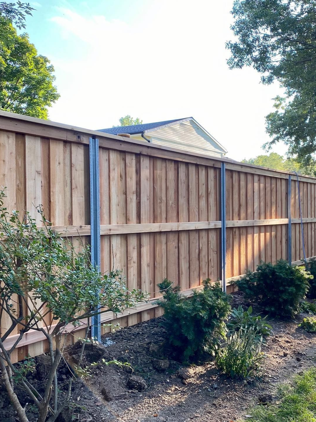 Light brown wooden fence corner enclosing a square area with vertical planks.