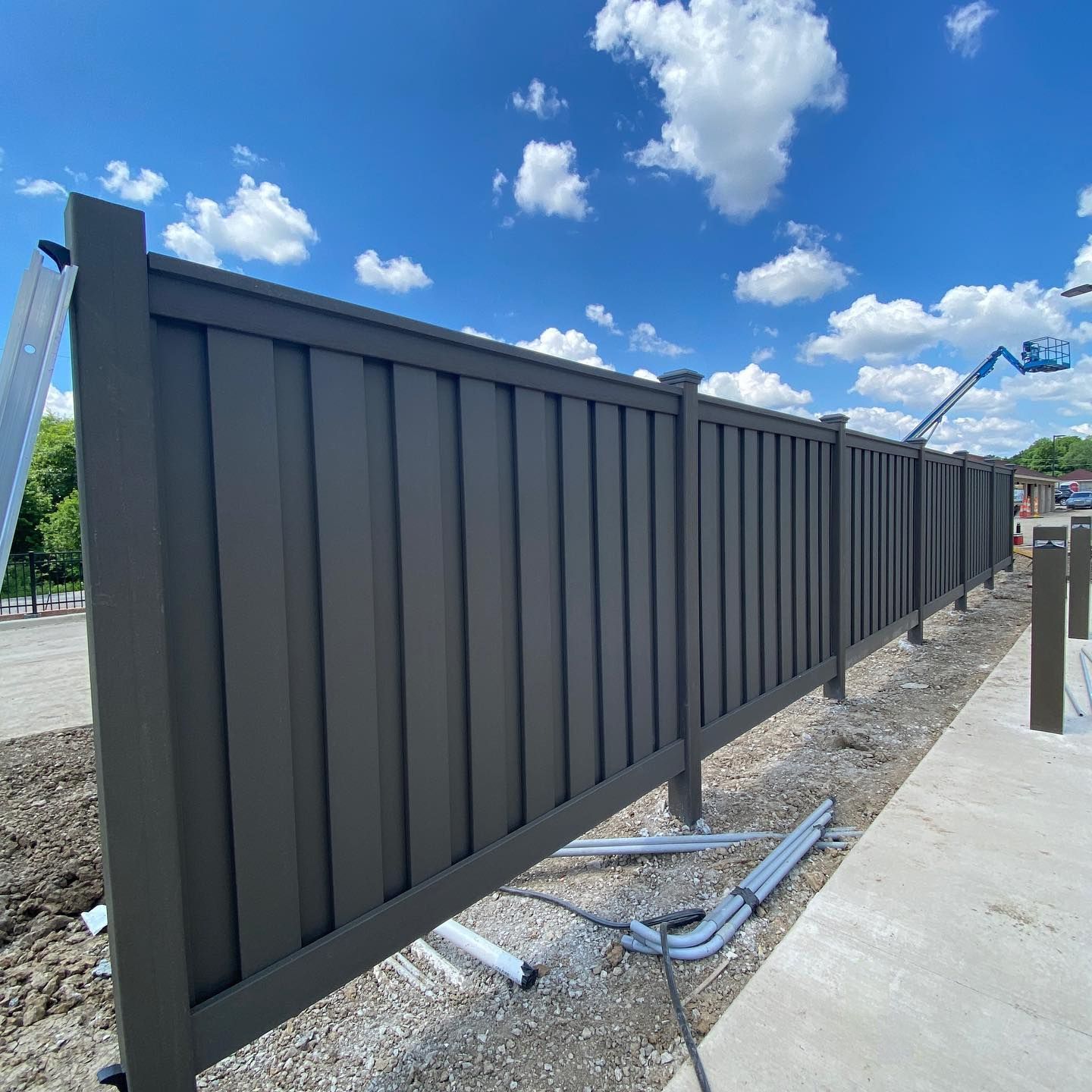 Gray privacy fence under a blue sky with some construction materials nearby.