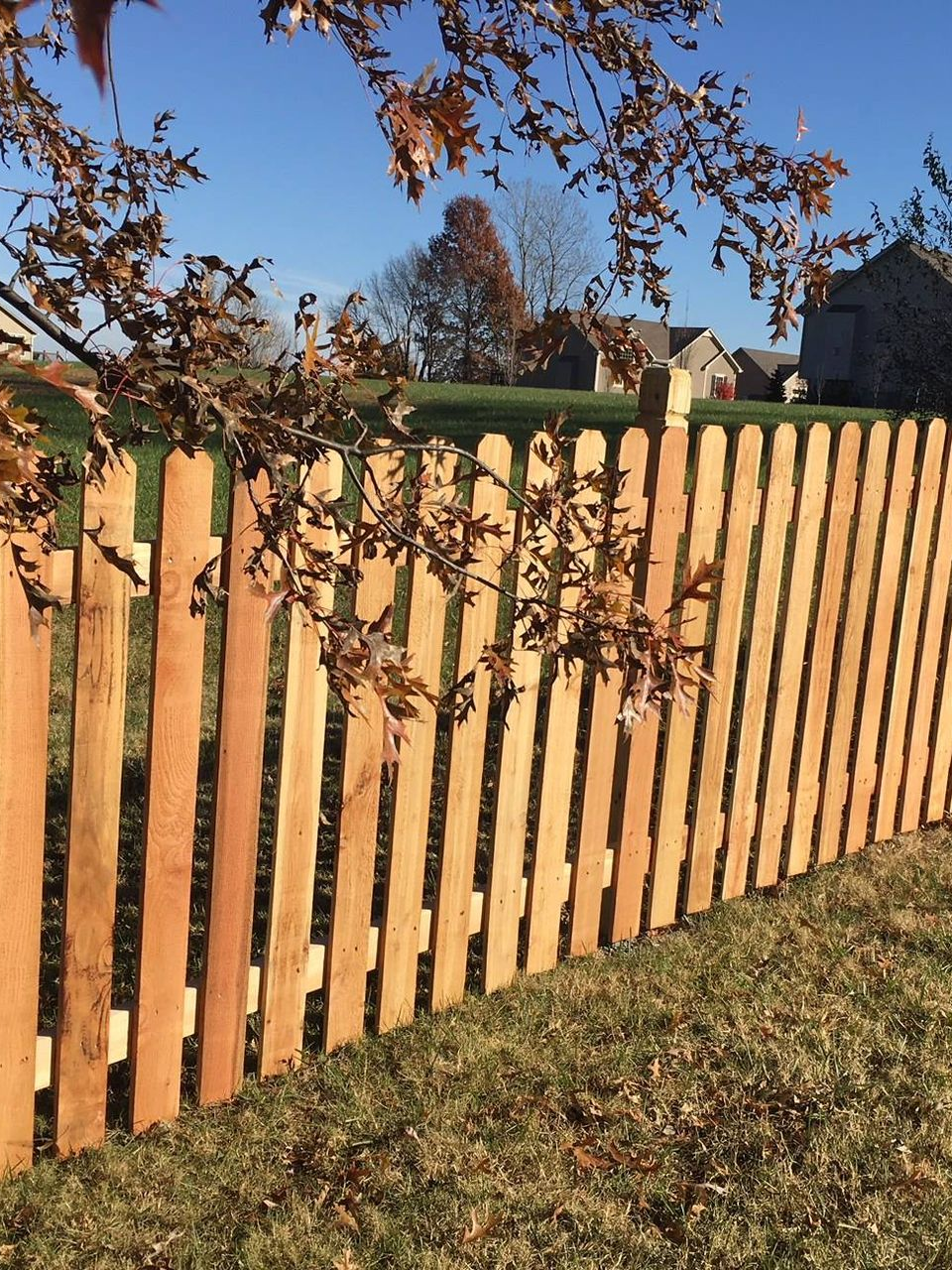 Light brown wooden fence corner enclosing a square area with vertical planks.