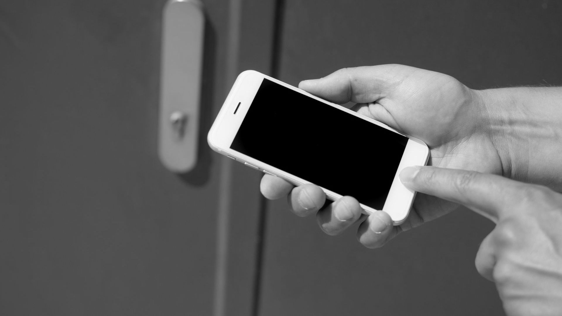 Hand holding a white smartphone, touching the screen, next to a gray door.