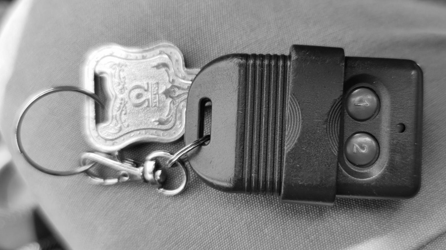 Keys and a garage door remote, on a person's lap. Black and silver.