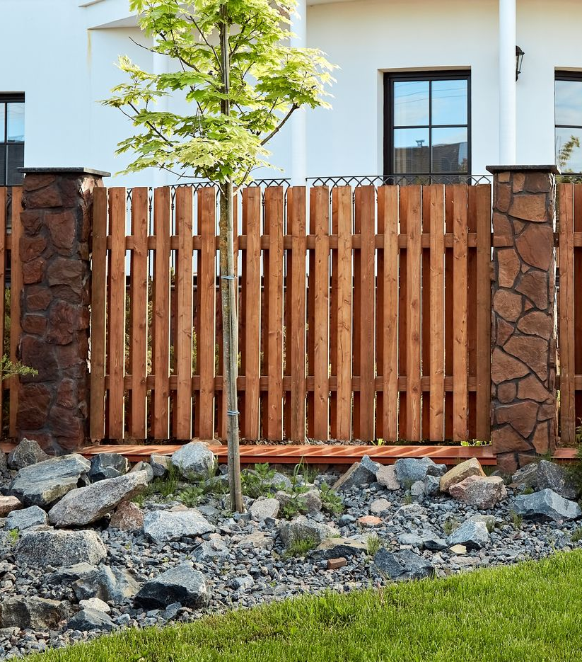 Light brown wooden fence corner enclosing a square area with vertical planks.