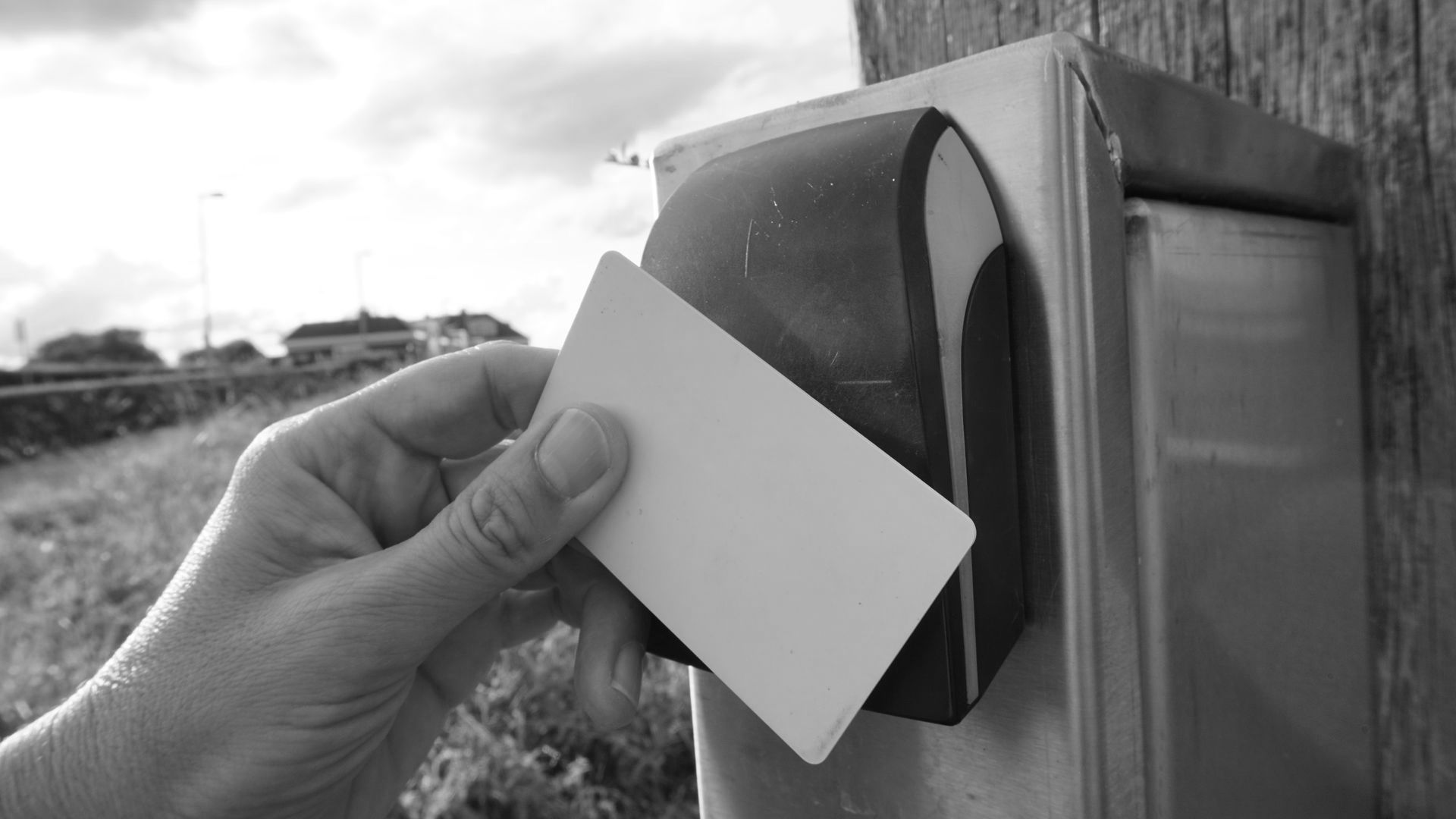 Hand holding a white card near a card reader attached to a wooden post.