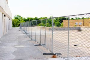 Chain-link fence along a concrete path, separating it from a construction site.