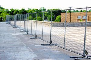 Chain link fence erected on a concrete surface, likely a parking area or construction site.
