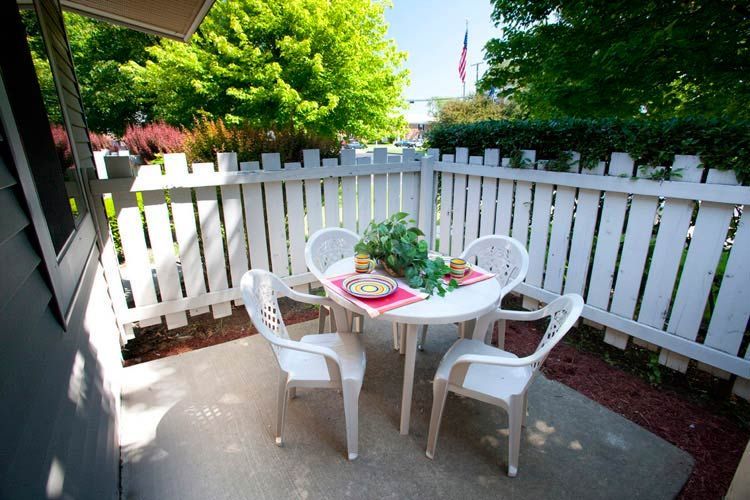 A patio with a table and chairs and a white picket fence