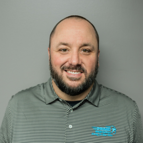 Man with a beard smiling, wearing a gray striped polo shirt with a company logo, in front of a gray wall.