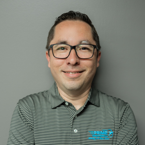 Man wearing glasses, striped shirt, smiling in front of a gray wall.