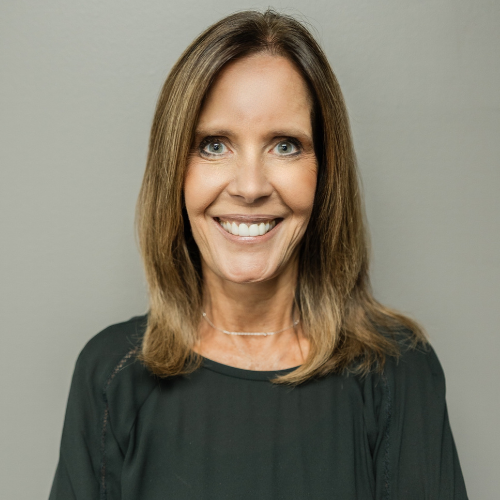 Woman smiling at the camera, wearing a dark green top, against a gray backdrop.