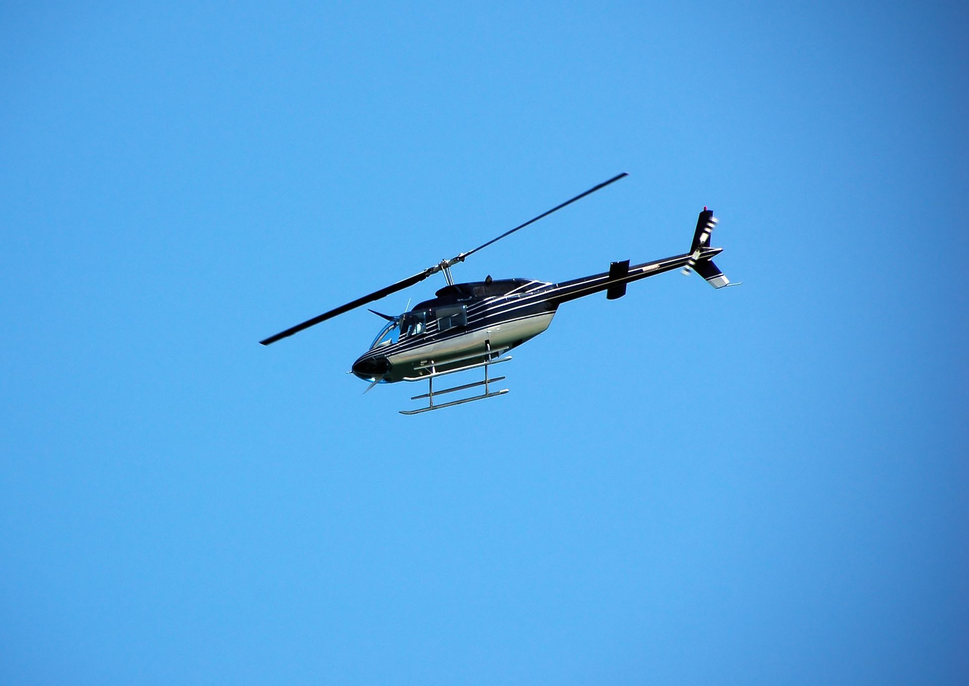Helicopter with a black and silver pattern against a clear blue sky.