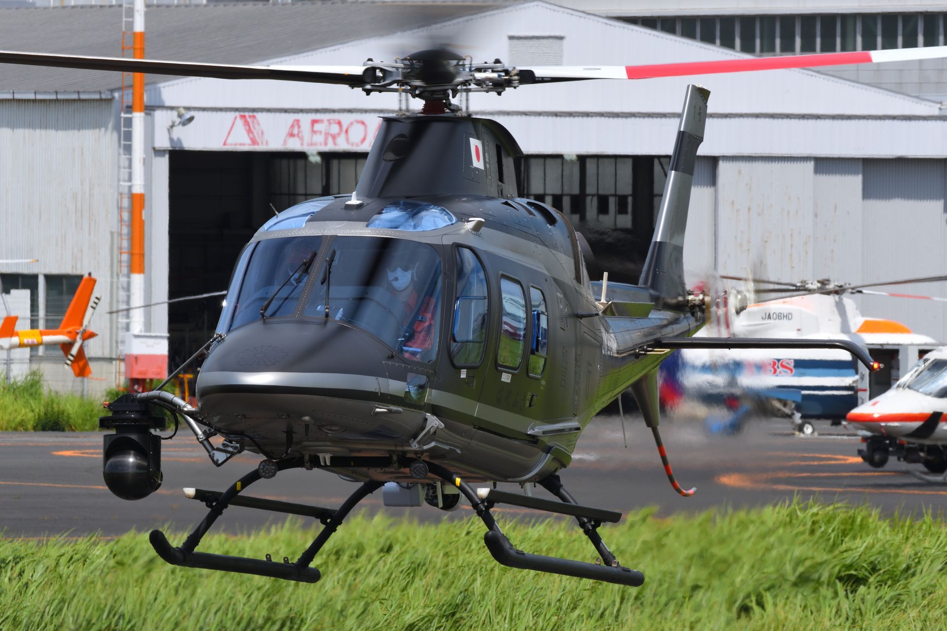 Black helicopter with silver trim taking off near a hangar.