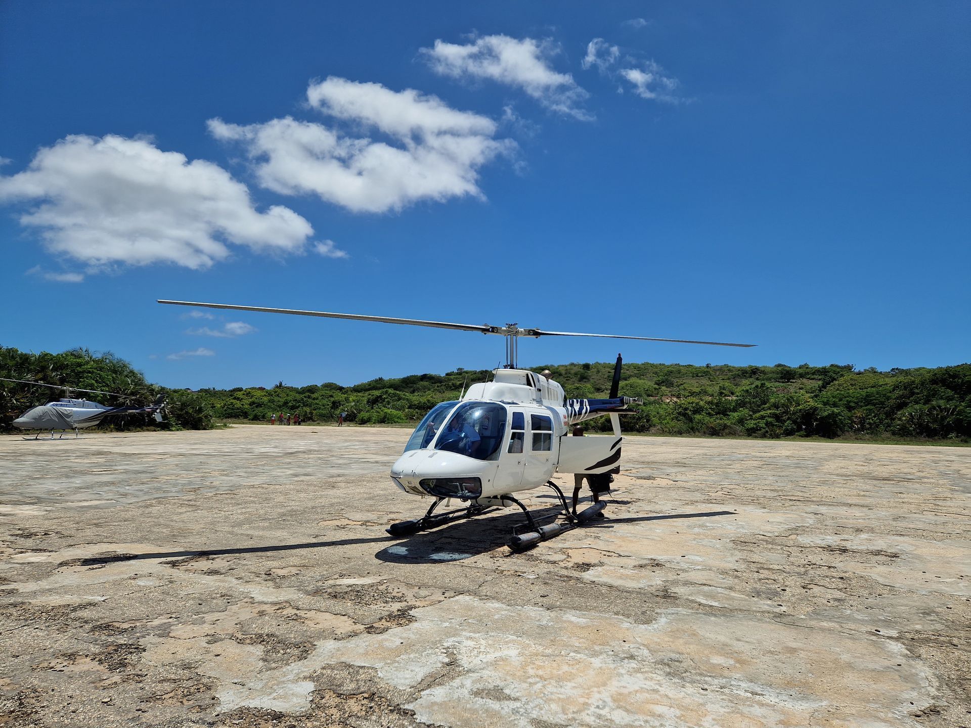 White helicopter on a rocky landing pad under a blue sky with scattered clouds.