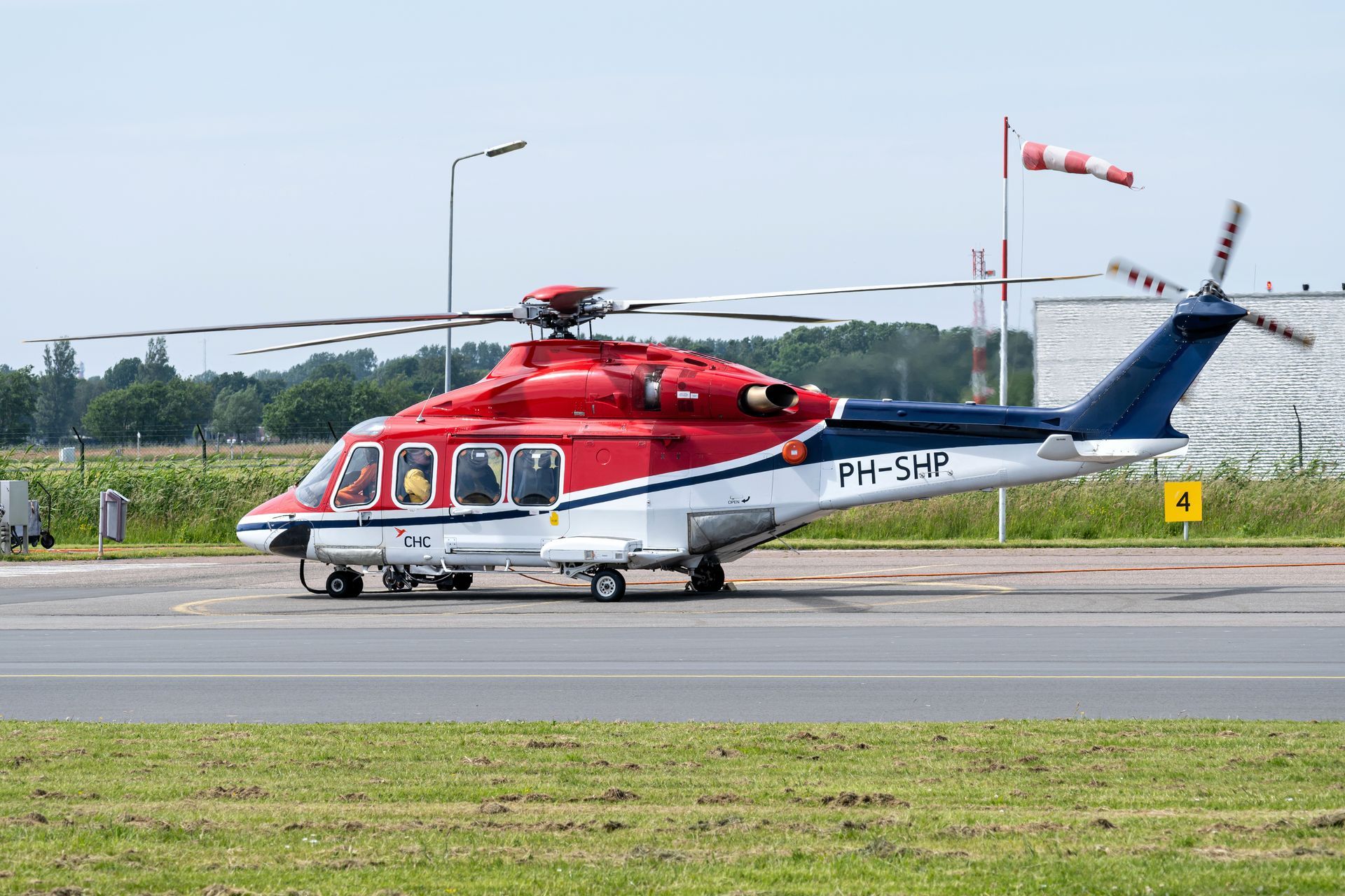 White, red, and blue helicopter in flight over city buildings.