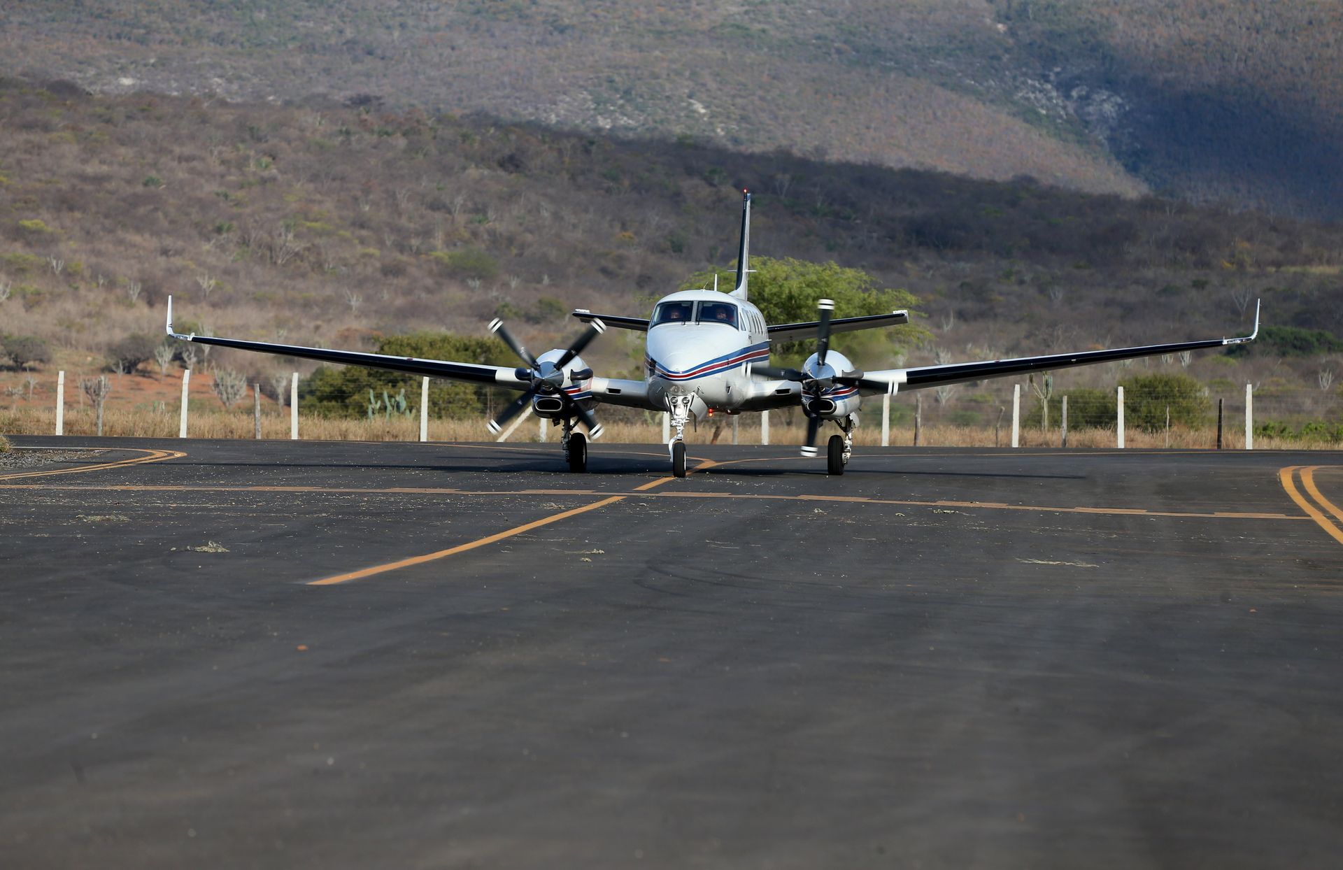 Yellow agricultural aircraft in flight, spraying chemicals with blue and yellow accents against a cloudy sky.