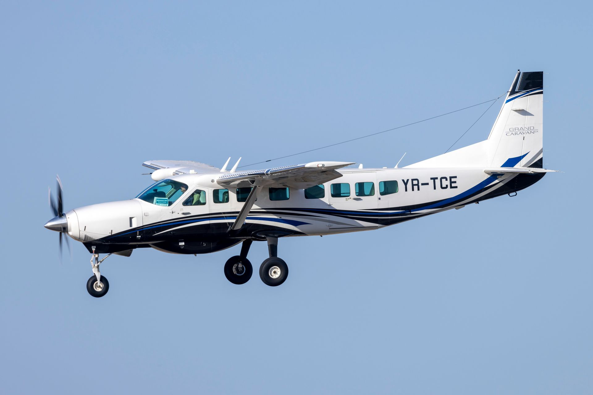White and black Cessna airplane in flight, against a clear blue sky.